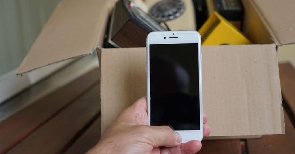 A hand holding an old smartphone over a box of electronics
