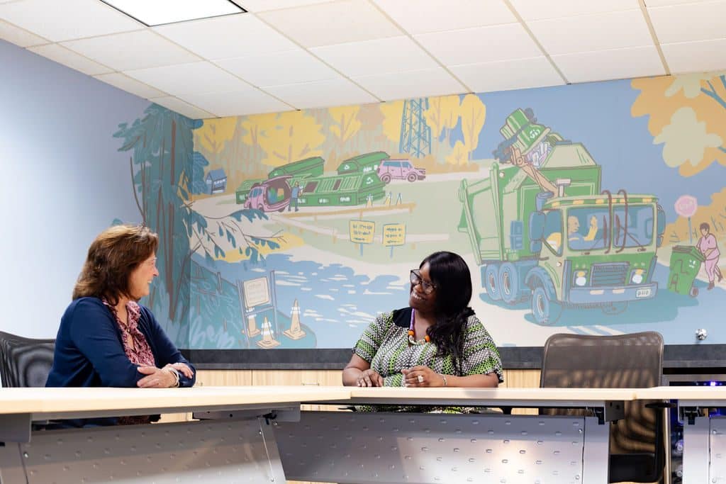 Two CVWMA staff members talk in front of a recycling-truck mural at the CVWMA office